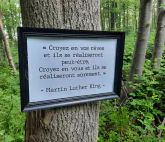 A sign on a tree cites Martin Luther King in French: “Croyez en vos rêves et ils se réaliseront peut-être. Croyez en vous et ils se réaliseron sûrement.”